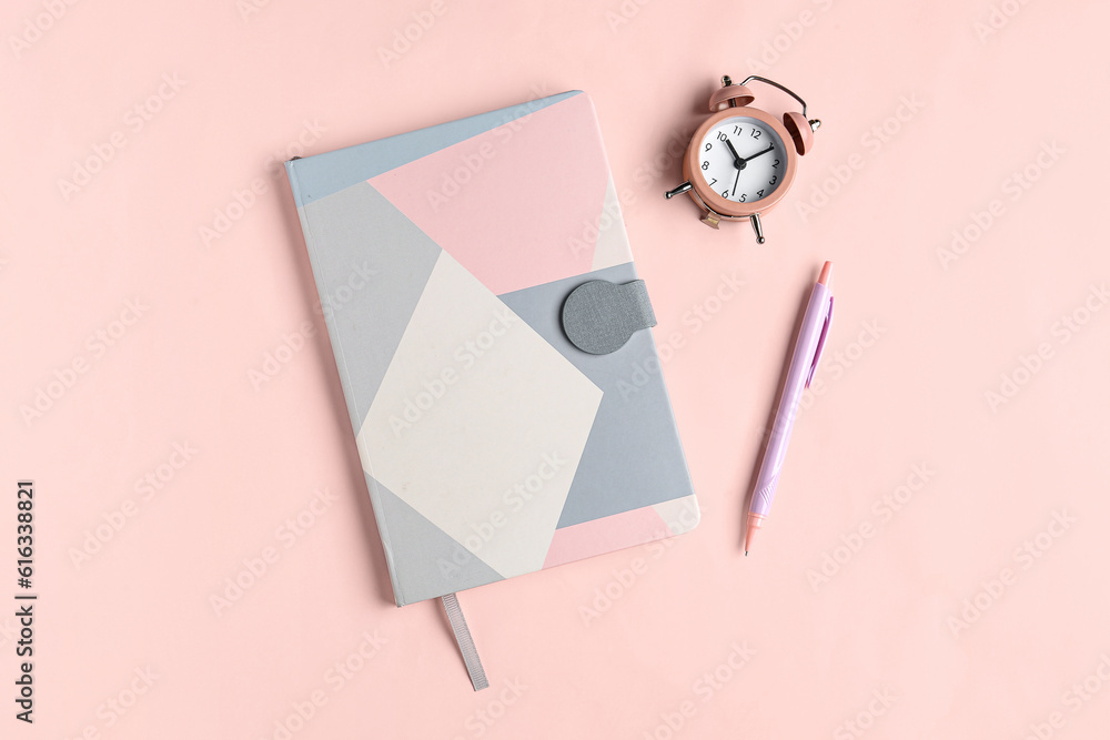 Notebook, pen and alarm clock on pink background