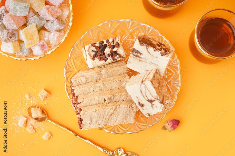 Pieces of tasty marble halva, Turkish delight and glasses with tea on orange background