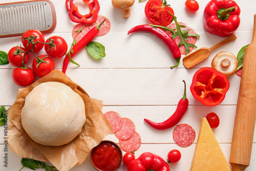 Frame made of raw dough and ingredients for preparing pizza on light wooden background