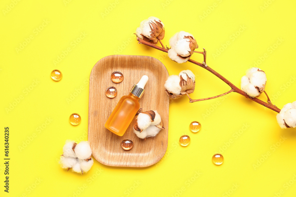 Composition with bottle of essential oil, glass stones and cotton flowers on yellow background