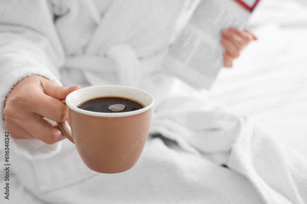 Woman in bathrobe holding cup of delicious coffee, closeup