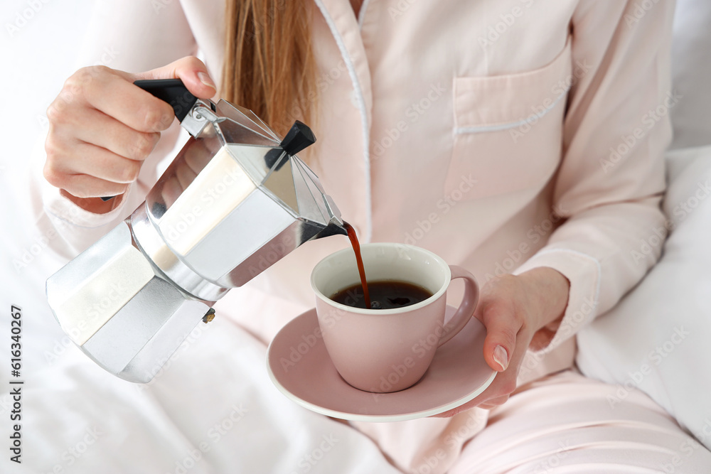 Woman pouring espresso from geyser coffee maker into cup in bed