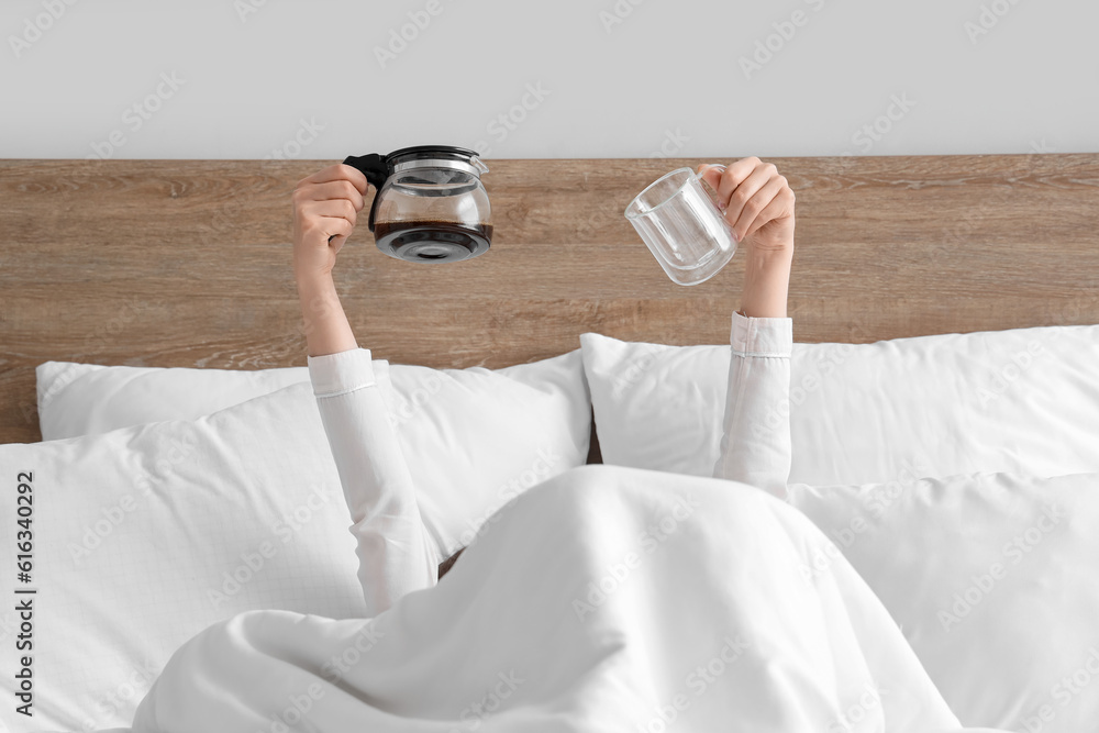 Woman holding coffee pot and empty cup in bed