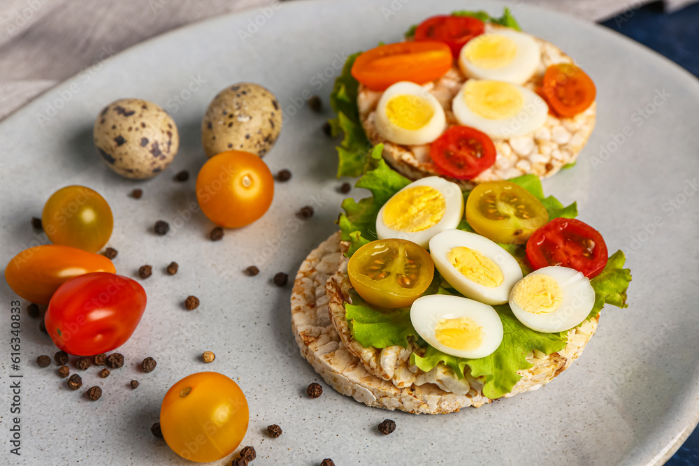 Rice crackers with quail eggs, tomatoes and lettuce on table, closeup