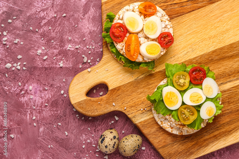 Rice crackers with quail eggs, tomatoes and lettuce on pink background