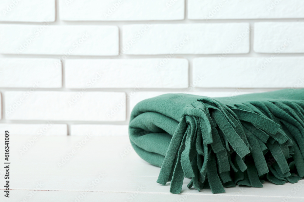 New soft folded blanket on table near light brick wall, closeup