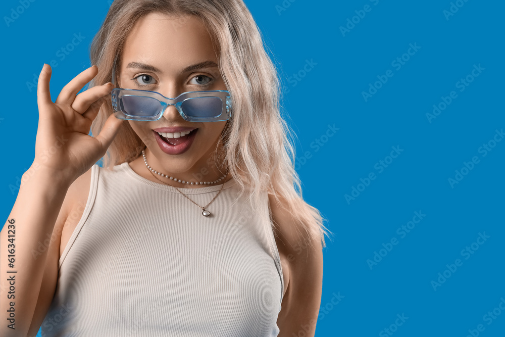 Young woman in stylish sunglasses on blue background, closeup