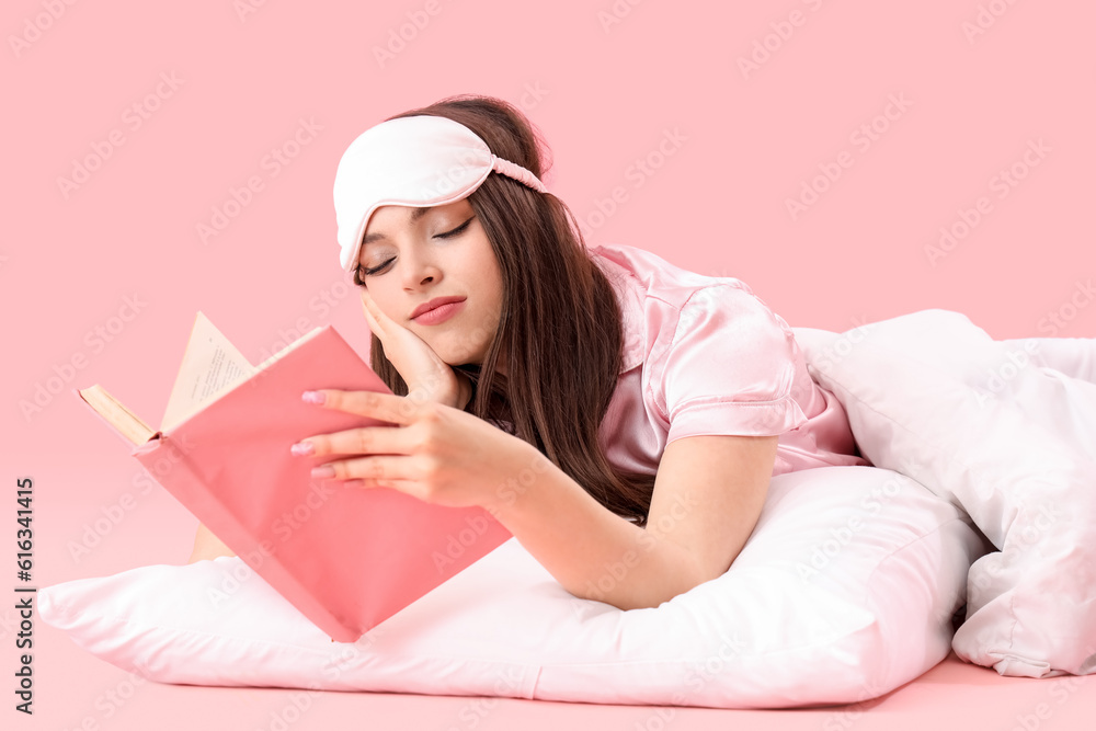 Young woman with soft blanket reading book on pink background