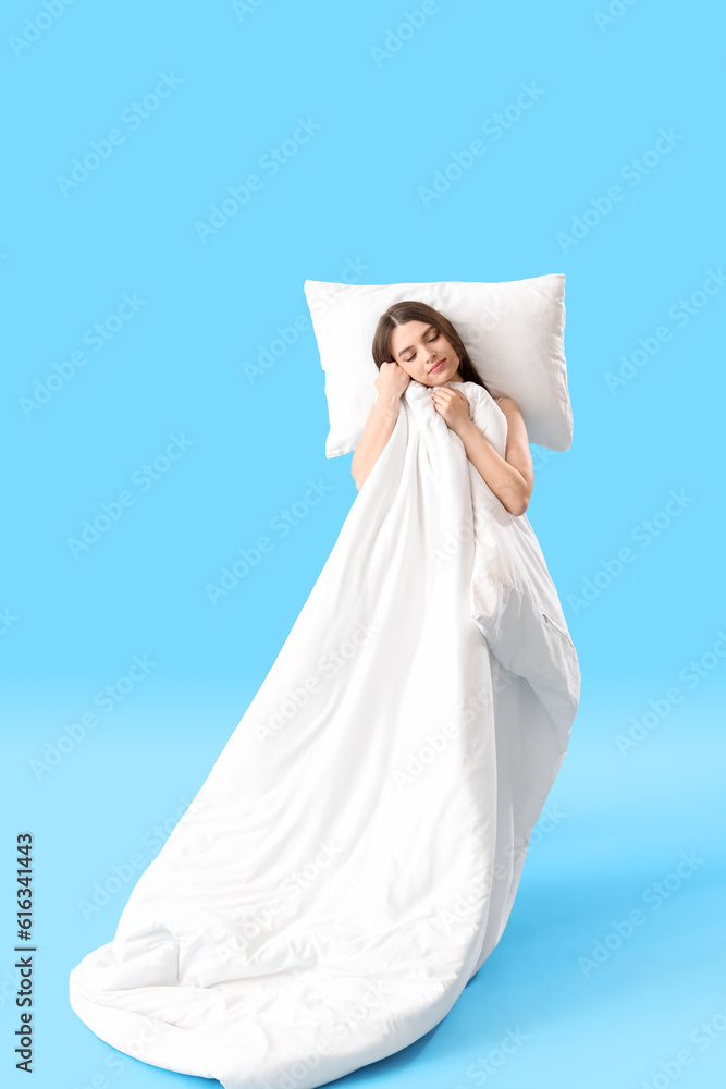 Young woman with soft pillow and blanket on blue background