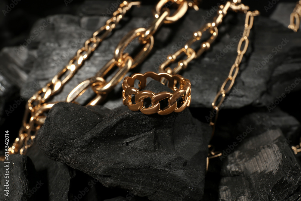 Beautiful chain bracelets and ring on black charcoal, closeup