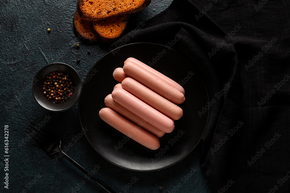 Plate with tasty thin sausages and peppercorn on dark background