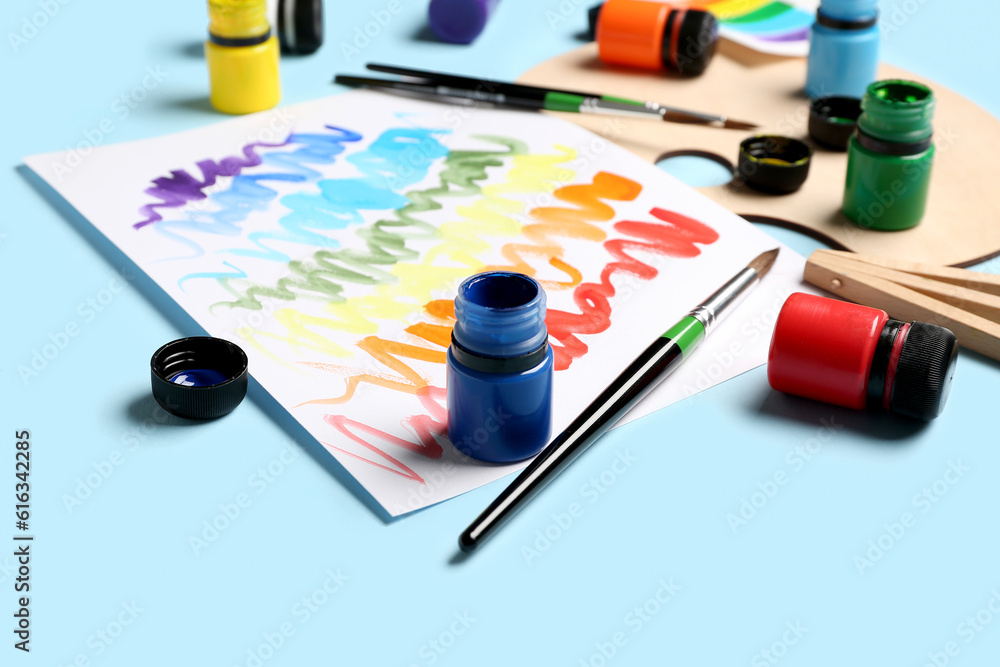 Composition with different paints, brushes and rainbow color palette on blue background