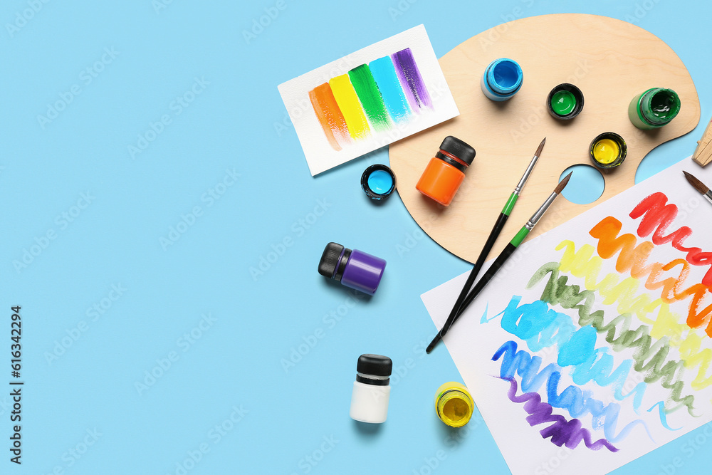 Composition with different paints, brushes and rainbow color palette on blue background