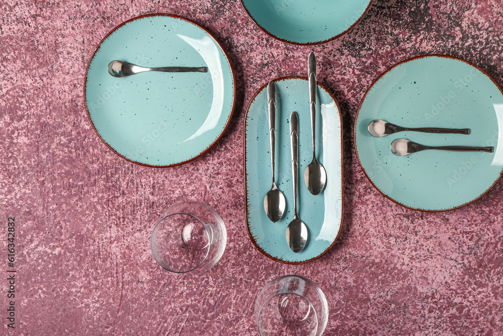 Clean plates, glasses and set of cutlery on dark pink table