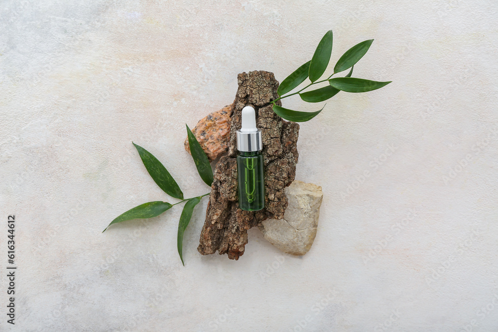 Bottle of cosmetic oil with leaves and tree bark on white background