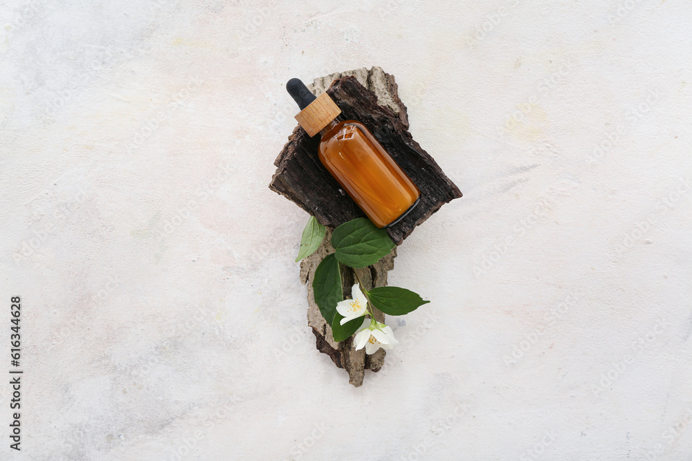 Bottle of cosmetic oil with jasmine flowers and tree bark on white background