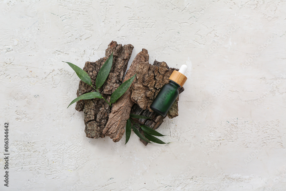 Bottle of cosmetic oil with leaves and tree bark on white background