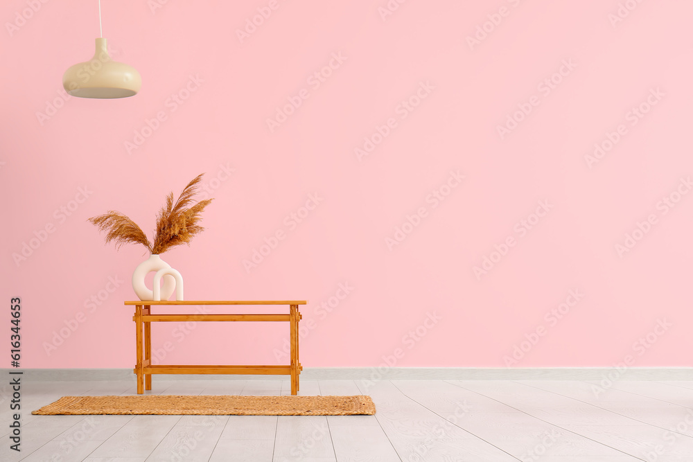 Wooden table with pampas grass in vase near pink wall