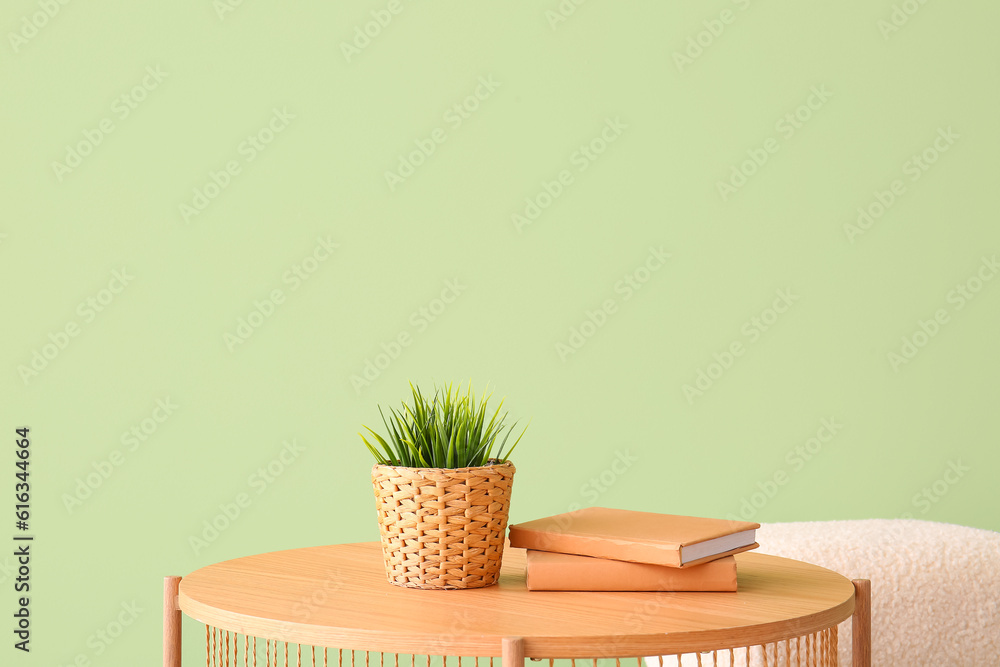 Wooden coffee table with houseplant, books and pouf near green wall