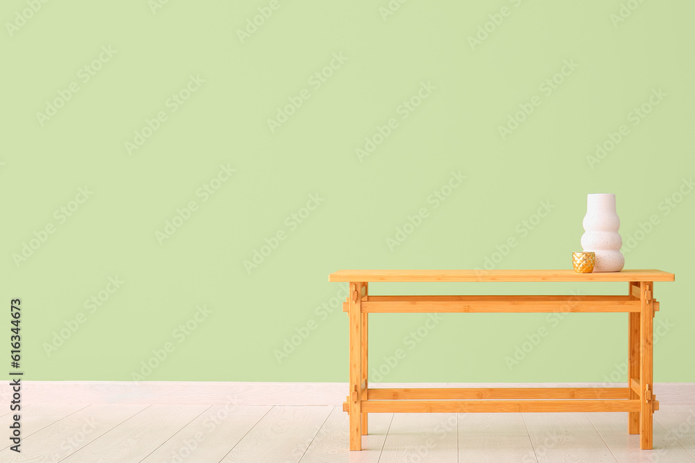 Wooden table with vase and cup near green wall