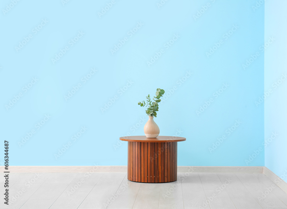 Wooden coffee table with eucalyptus branches in vase near blue wall