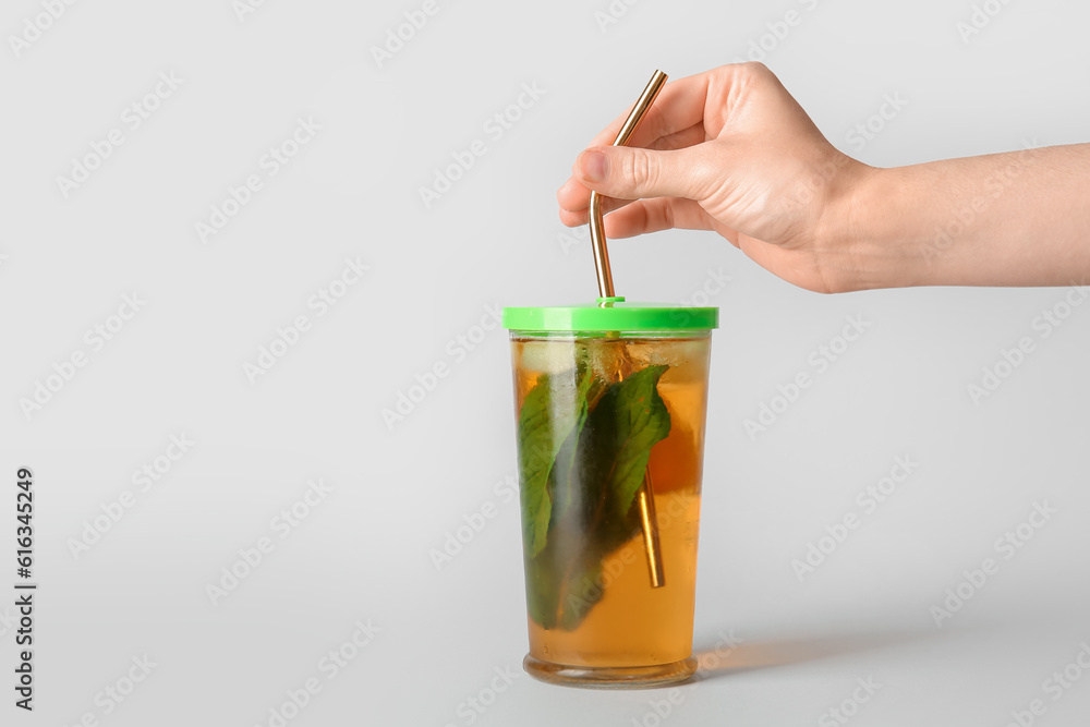 Woman putting straw into glass of ice tea with mint and lemon on white background