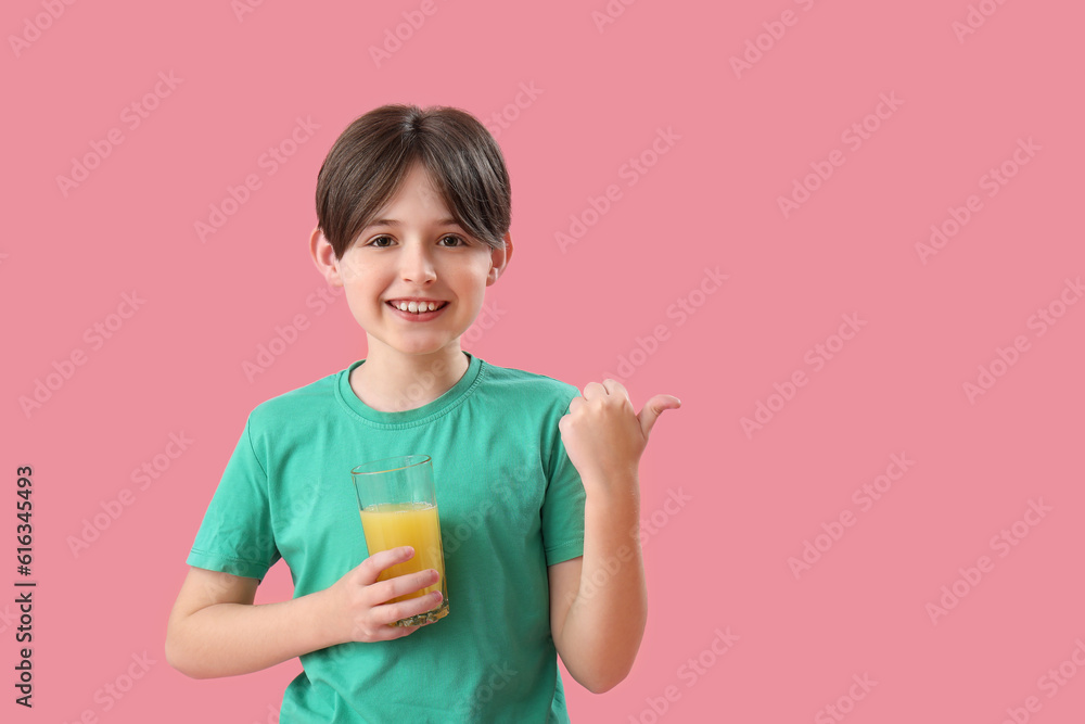 Little boy with glass of orange juice pointing at something on pink background