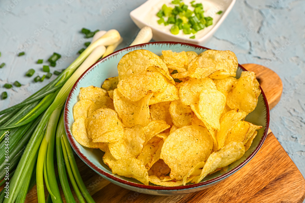 Bowl of tasty sour cream with sliced green onion and potato chips on blue background