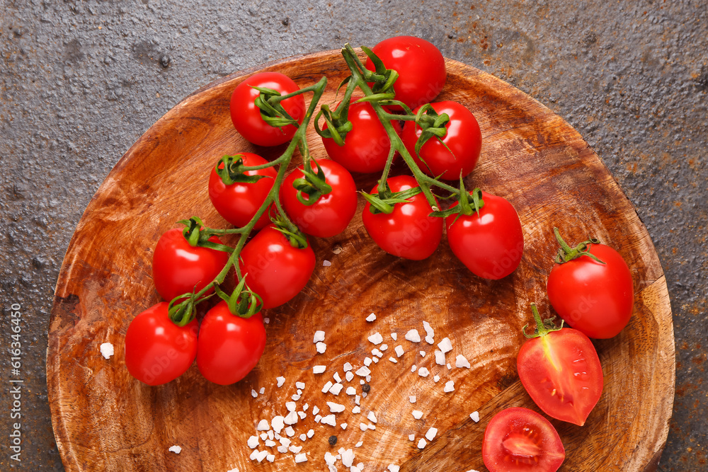 Wooden plate with fresh cherry tomatoes on dark background