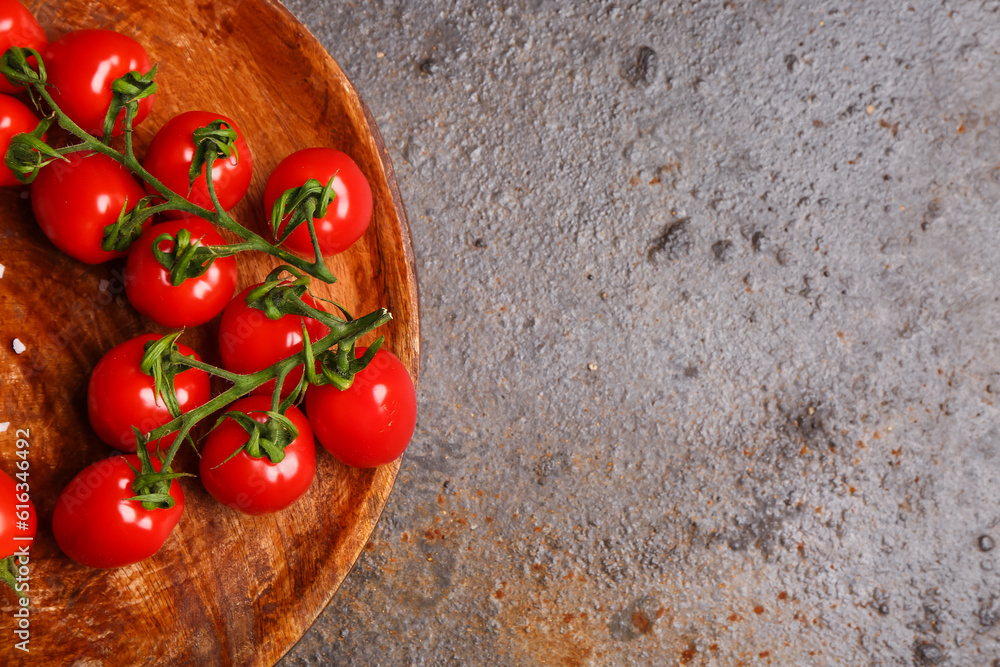 Wooden plate with fresh cherry tomatoes on dark background