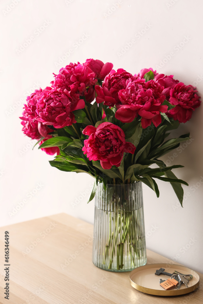 Vase of red peonies on dresser near light wall