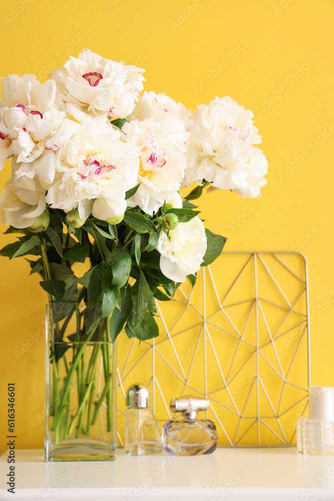 Vase of white peonies with perfumes on table near yellow wall