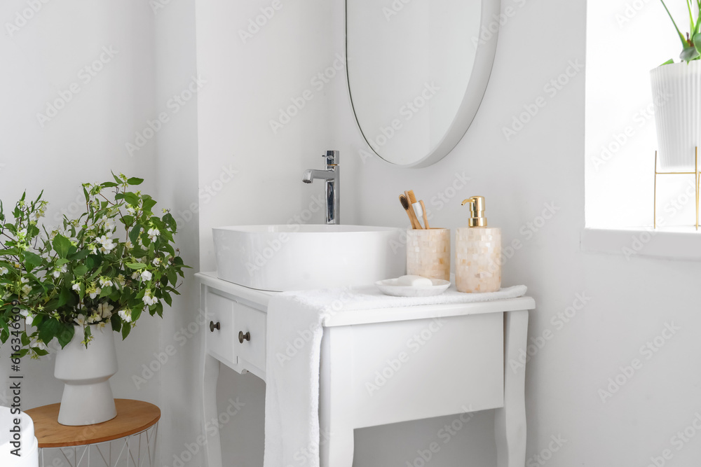 Sink bowl and bath accessories on dressing table in interior of light bathroom