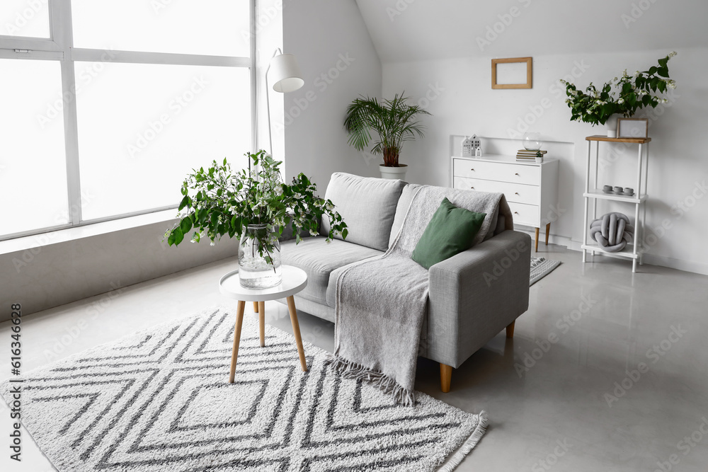 Grey sofa and vase with blooming jasmine flowers on coffee table in living room