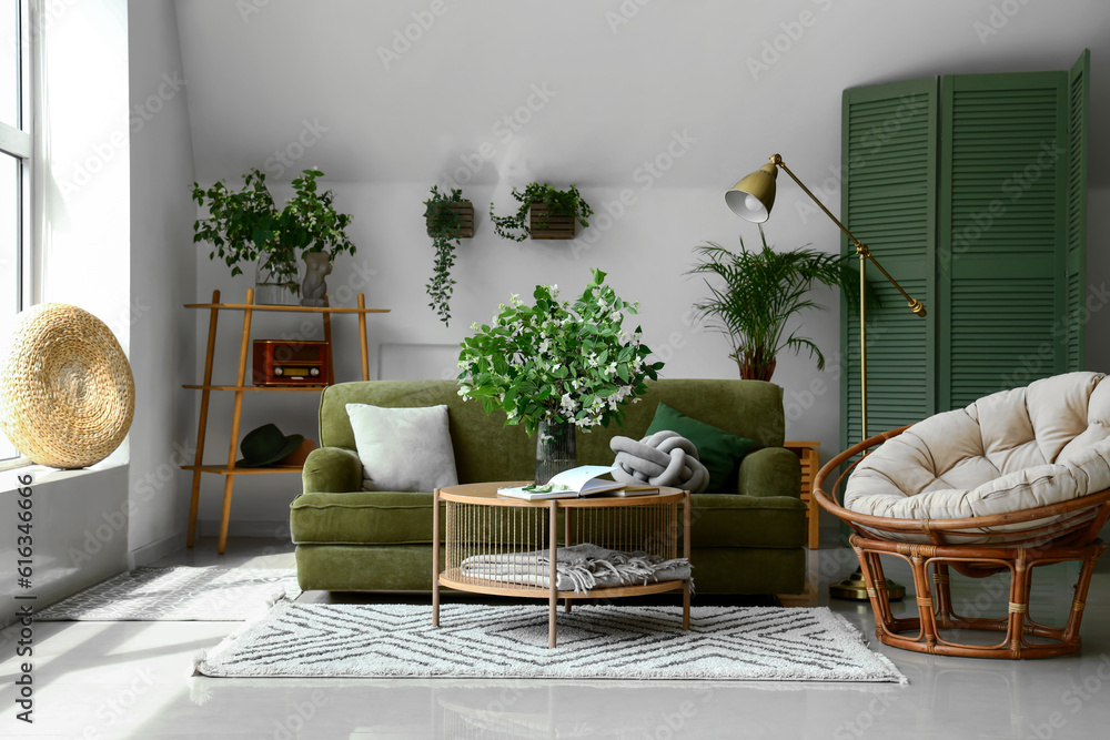 Interior of light living room with green sofa and blooming jasmine flowers on coffee table