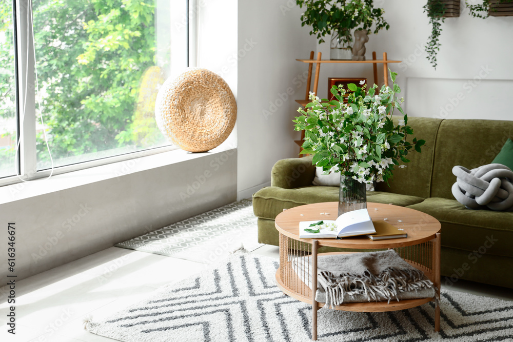 Interior of light living room with green sofa and blooming jasmine flowers on coffee table