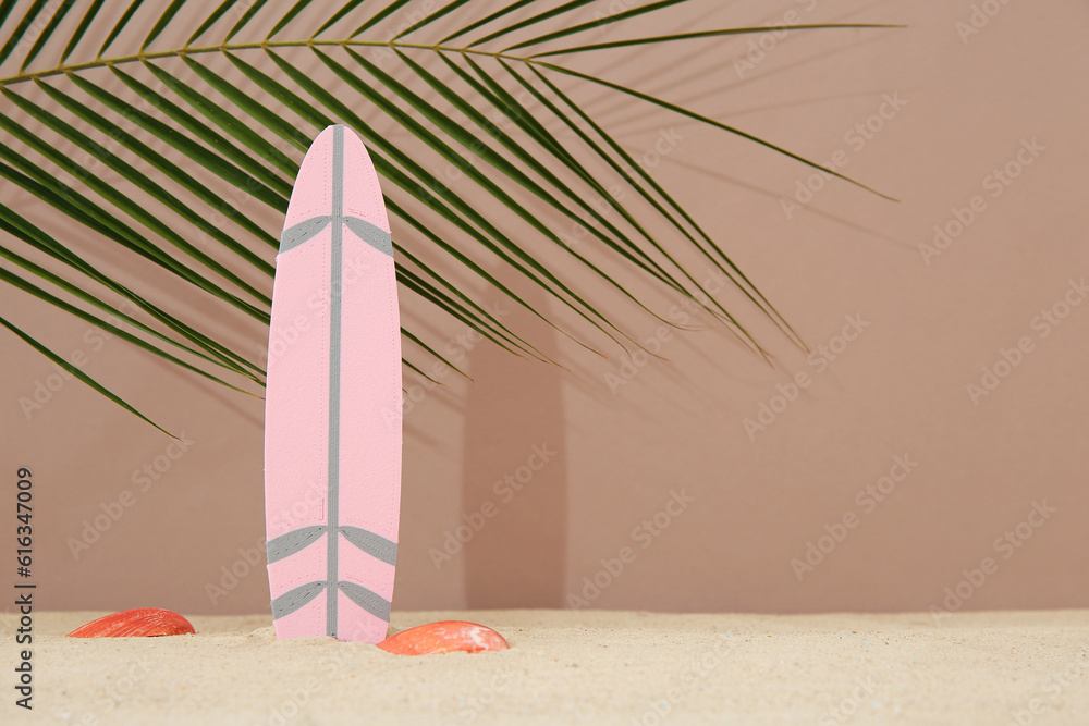 Mini surfboard with seashells and palm leaf on sand against brown background