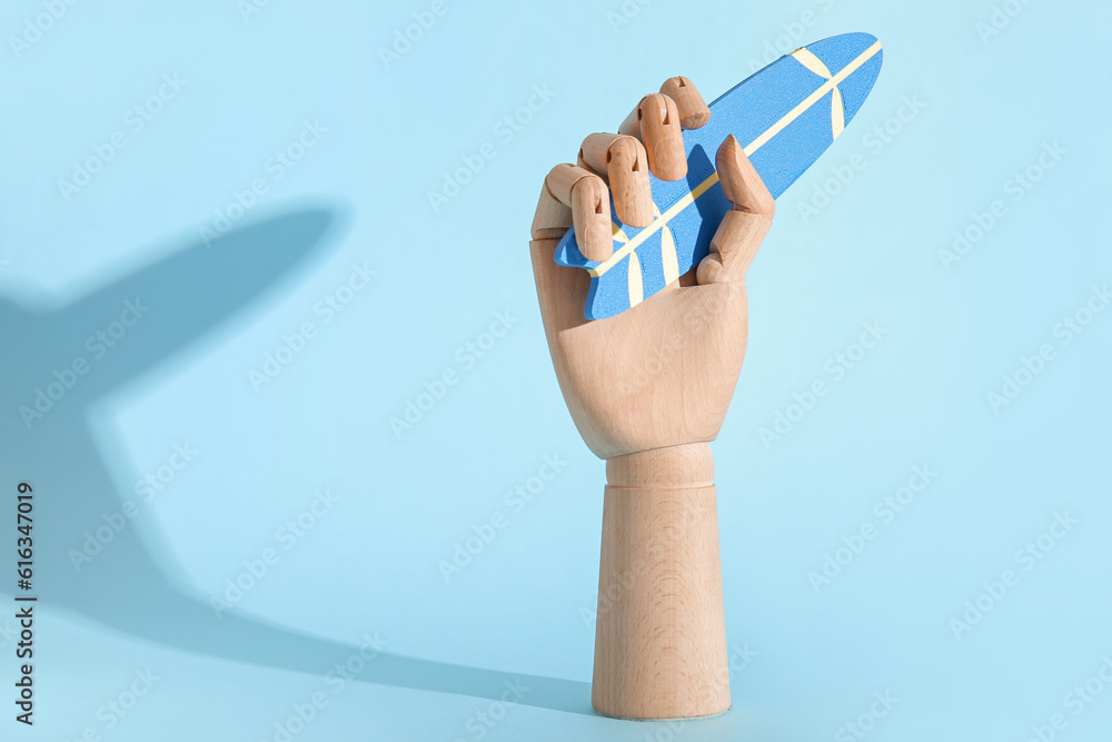 Wooden hand with mini surfboard on blue background