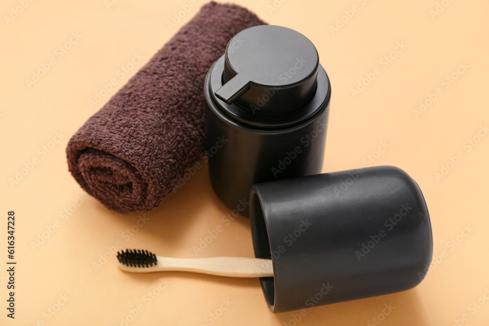 Holder with toothbrush, towel and bottle of cosmetic product on color background