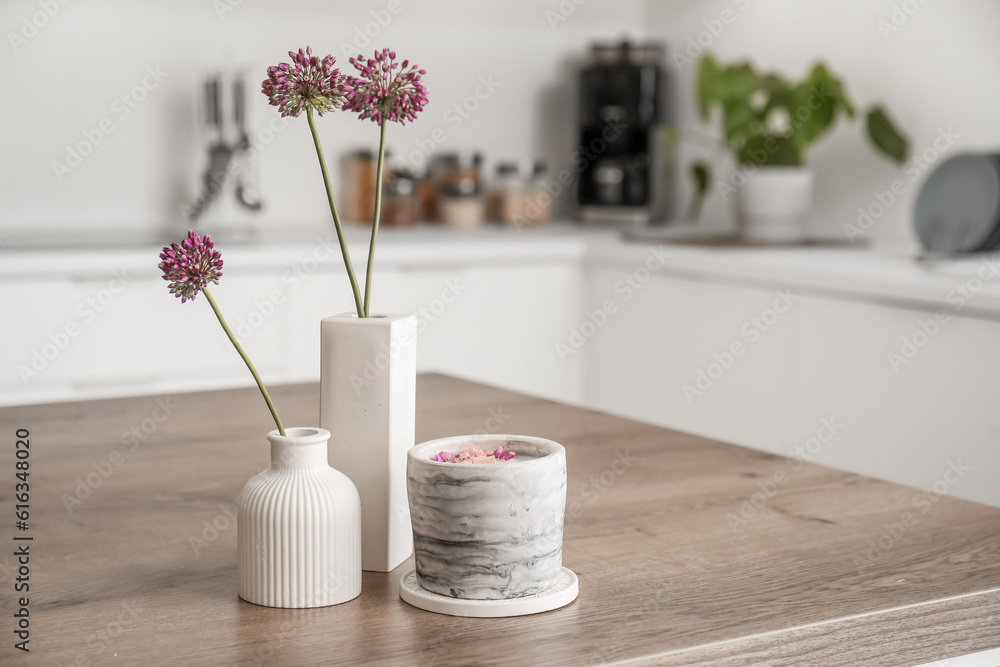 Beautiful flowers and candle on table in light kitchen, closeup