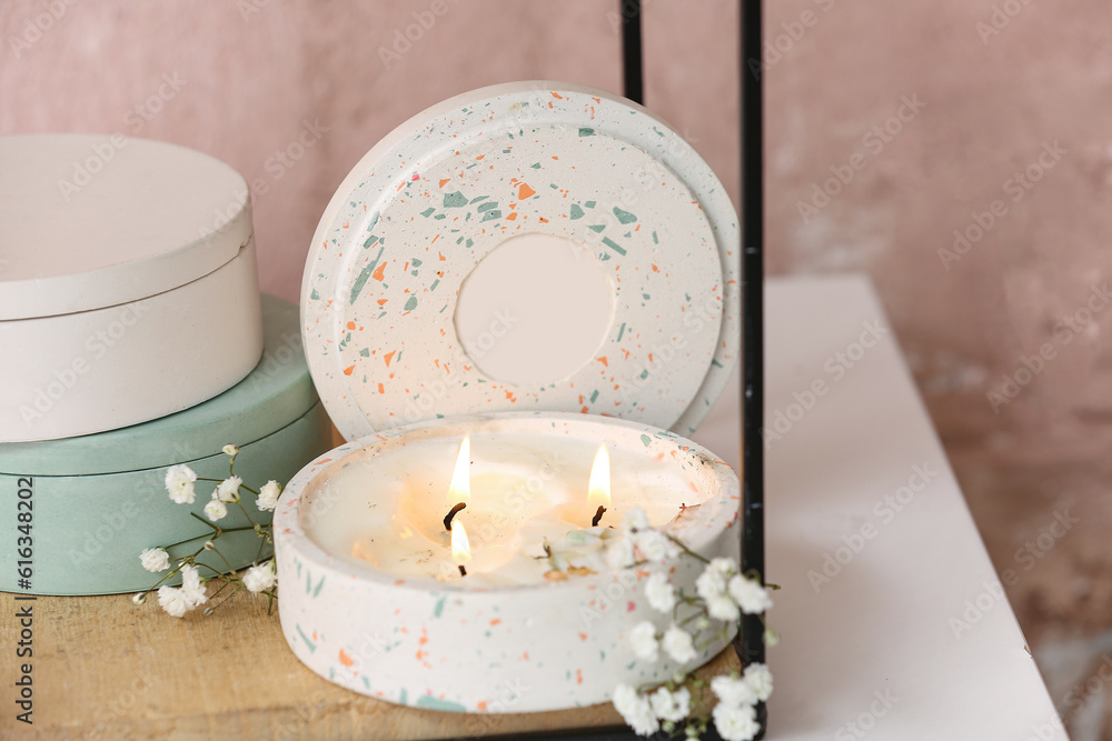 Gypsophila flowers and holder with burning candle on table in room, closeup