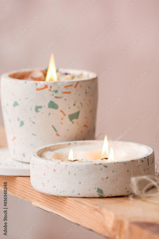 Holders with burning candles on wooden shelf in room, closeup