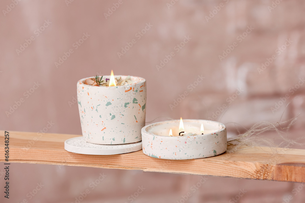 Holders with burning candles on wooden shelf in room, closeup