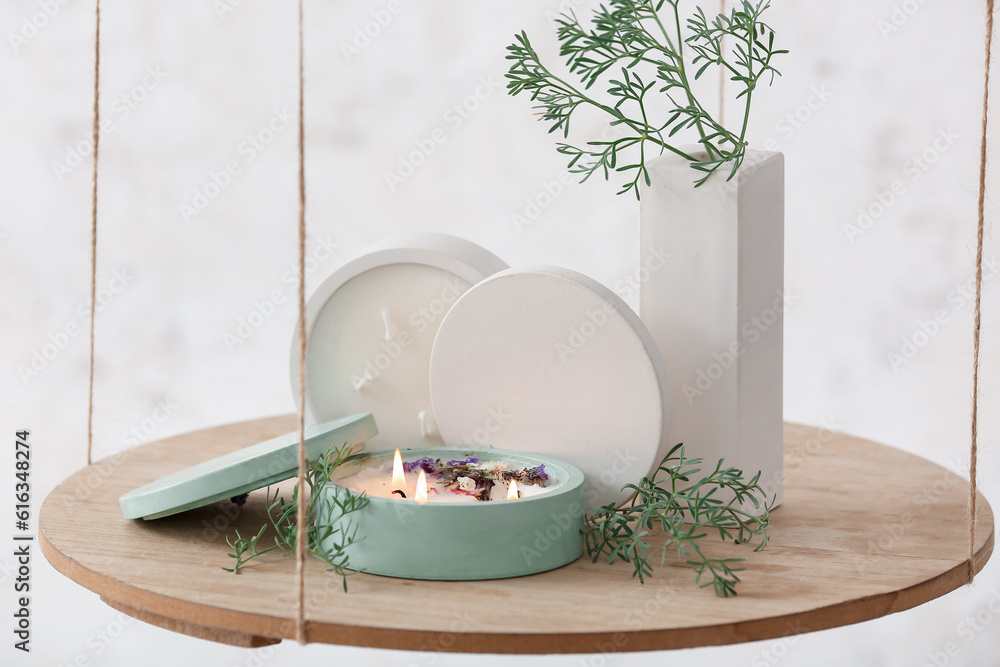 Fir tree branches and burning candle on hanging shelf near light wall in room, closeup