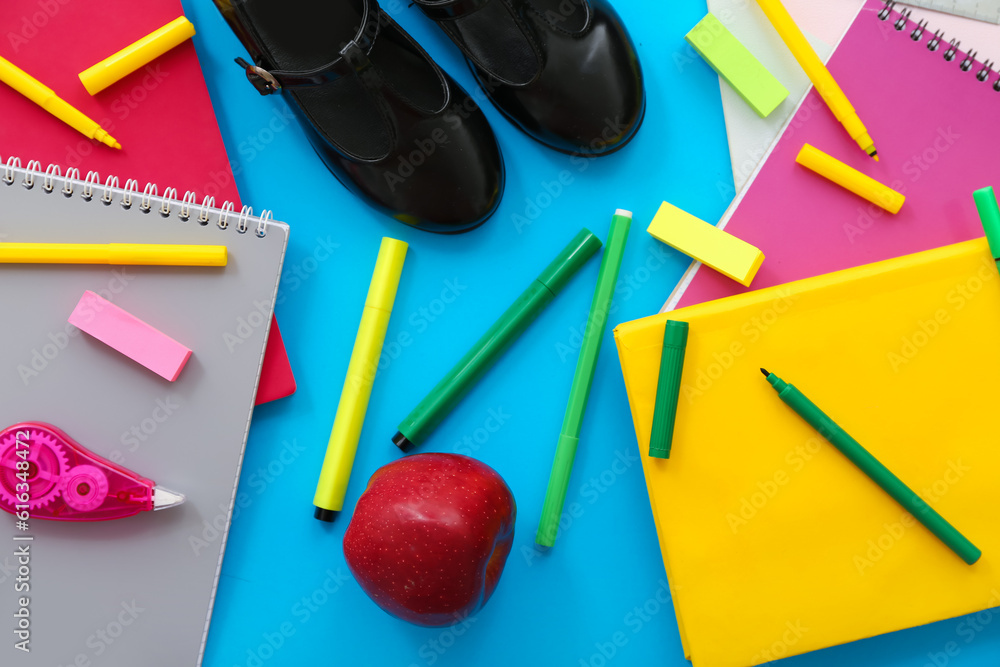 Stylish shoes with red apple and different stationery on blue background