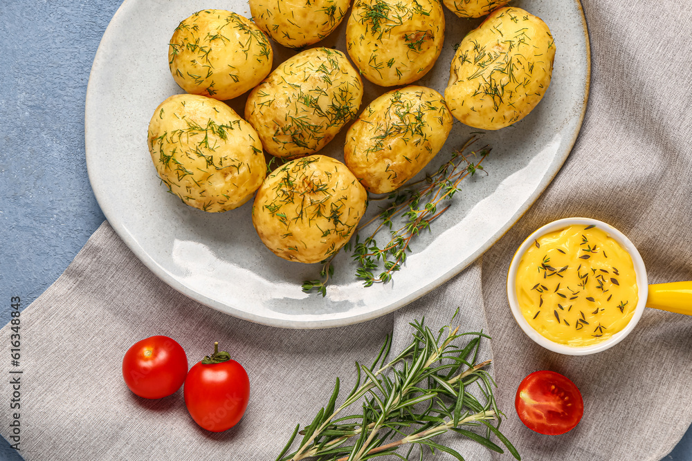 Plate of boiled baby potatoes with dill and tomatoes on blue background