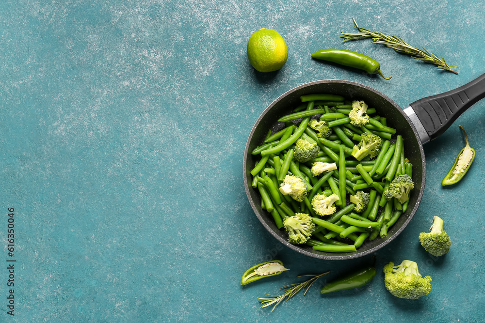 Frying pan with fresh vegetables on green background