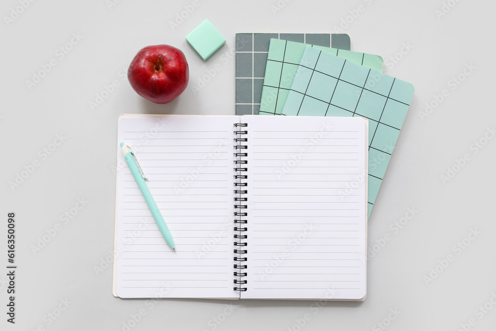 Notebooks with fresh red apple and stationery on grey background