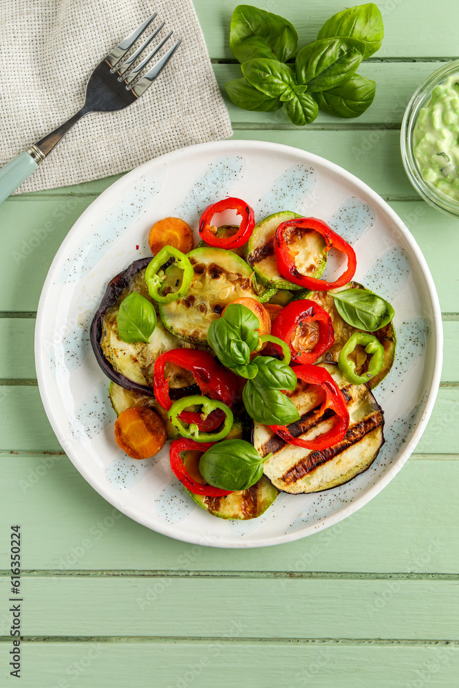 Plate with grilled vegetables and basil on green wooden table