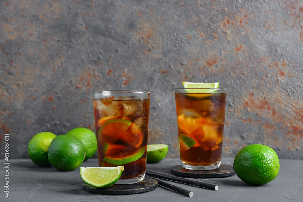 Glasses of cold Cuba Libre cocktail and limes on grey table